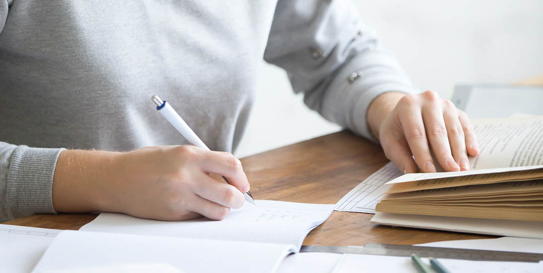 Profile portrait of a student girl performing a written task in a copybook, looking at the textbook, education concept photo