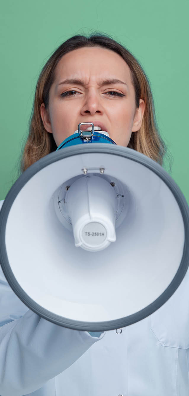 frowning young female doctor wearing medical robe and stethoscope around neck looking at camera talking by speaker isolated on blue background