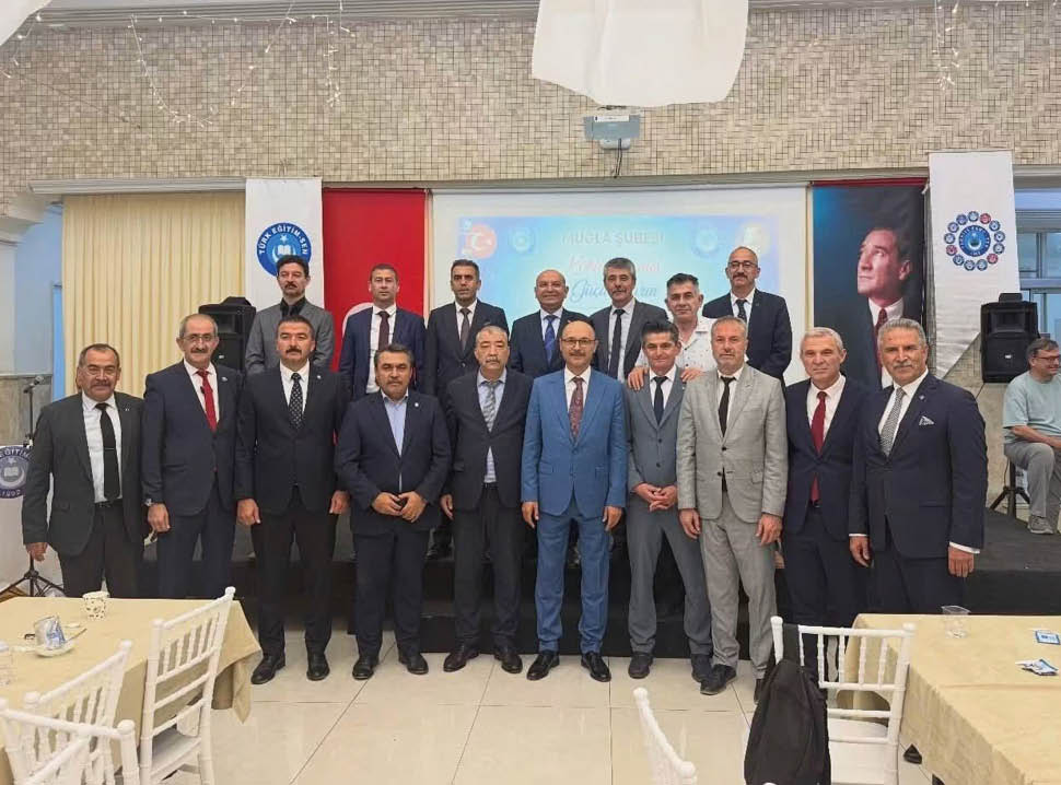 A group of formally dressed adults posing together indoors in front of a stage with banners and a screen. Description generated by AI