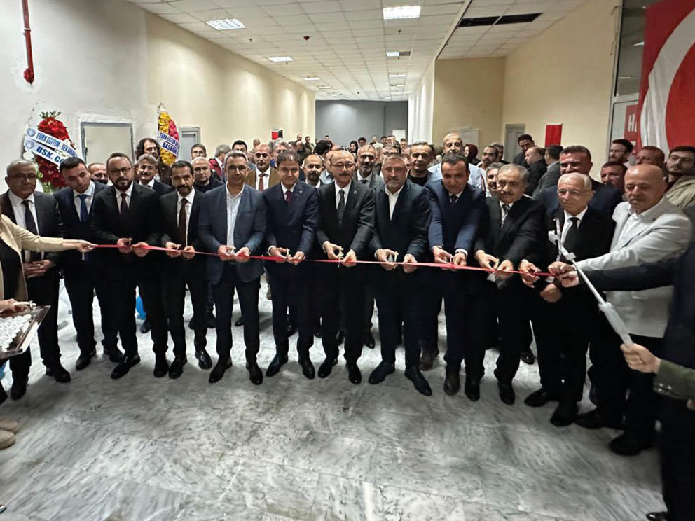 A group of formally dressed people stand in a hallway holding a long red ribbon for a ribbon-cutting ceremony. Description generated by AI