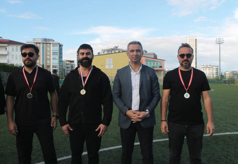 Four adults standing on a sports field with three wearing medals around their necks and one dressed in a blazer. Description generated by AI