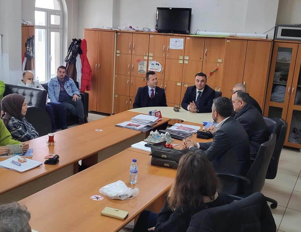 People in business attire are seated around a conference table in an office setting engaged in a meeting. Description generated by AI