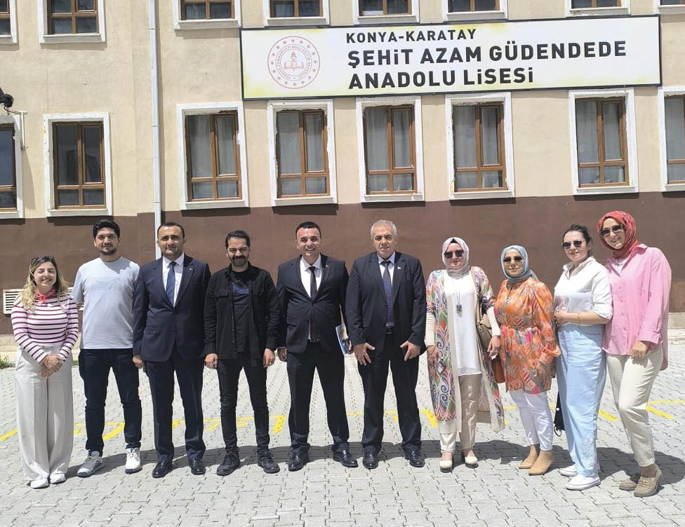 A group of people dressed in formal and casual clothing stand side by side outdoors in front of a building with windows and a sign above. Description generated by AI