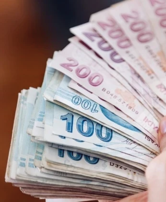 Hands holding a fanned-out stack of various denominations of currency notes. Description generated by AI