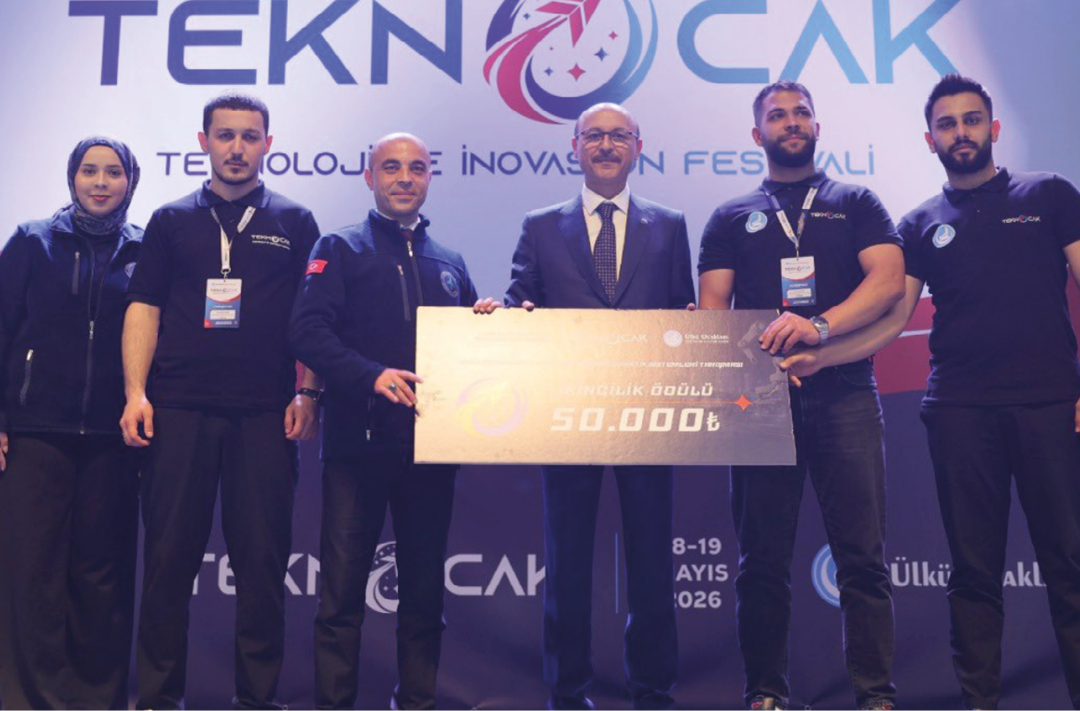 Six adults stand on a stage holding a large check with a technology festival backdrop behind them. Description generated by AI