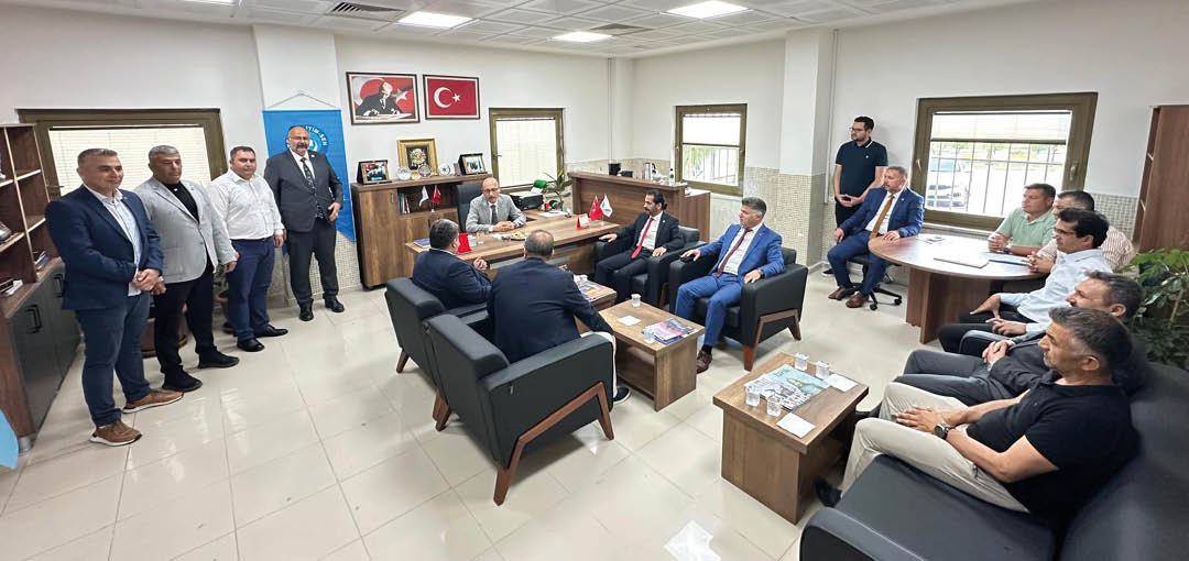 A group of people dressed in formal and casual attire are gathered in a well-lit office with modern furniture, engaged in a meeting or discussion. Description generated by AI