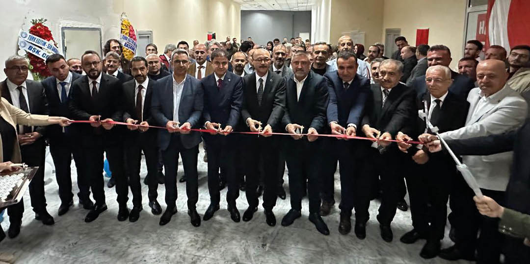 A group of formally dressed people stand in a hallway holding a long red ribbon for a ribbon-cutting ceremony. Description generated by AI