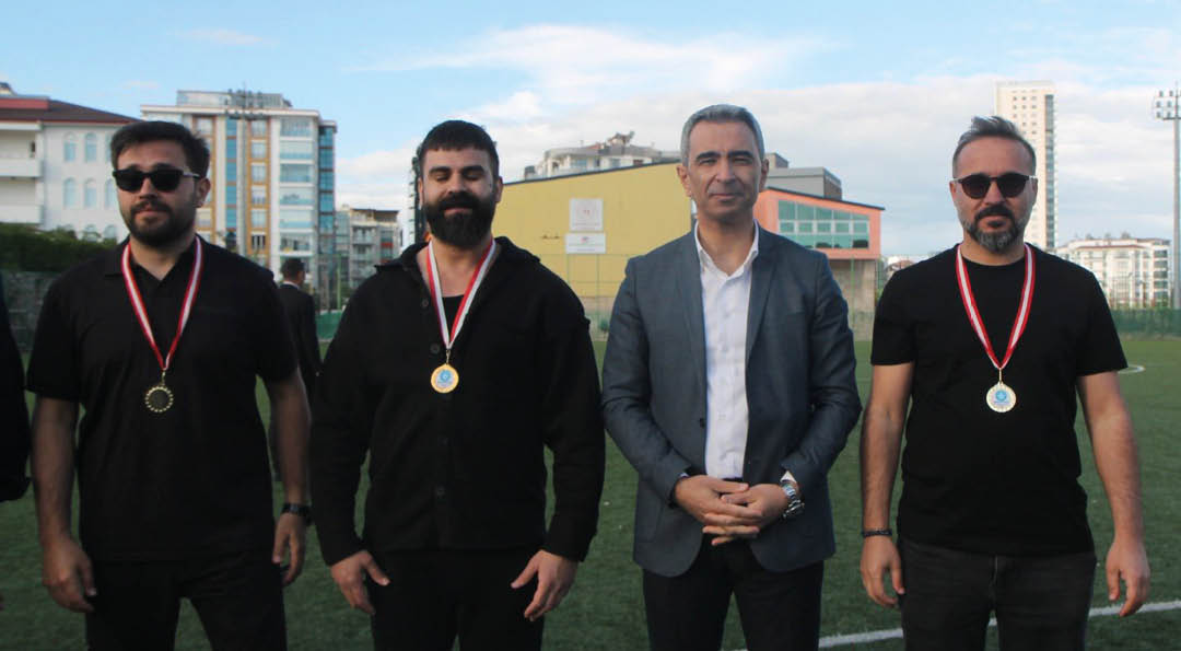 Four adults standing on a sports field with three wearing medals around their necks and one dressed in a blazer. Description generated by AI