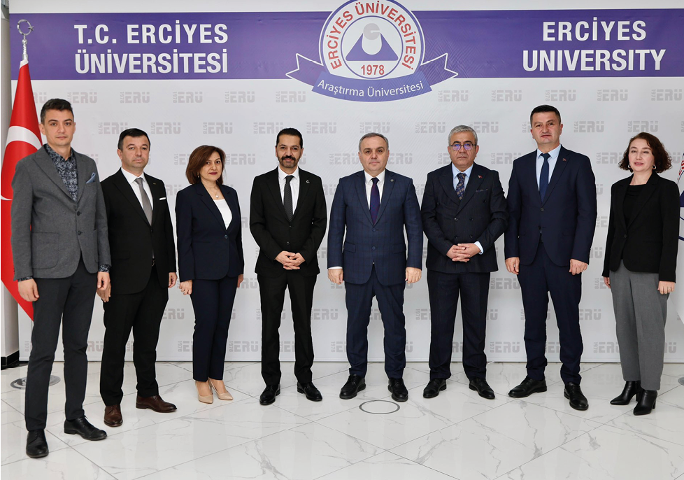 Five adults dressed in formal business attire stand side by side against a plain backdrop with a repeated logo pattern. Description generated by AI