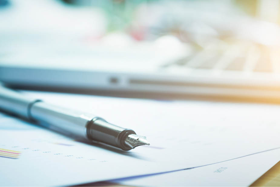 Closeup pen and blur background of computer on table in office.