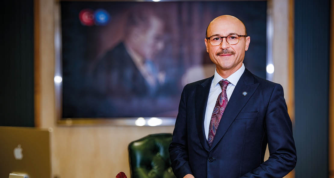 A man in a suit and tie standing in front of a picture. Description generated by AI