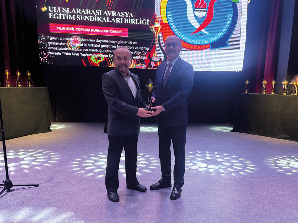 Two men standing on a stage holding an award. Description generated by AI