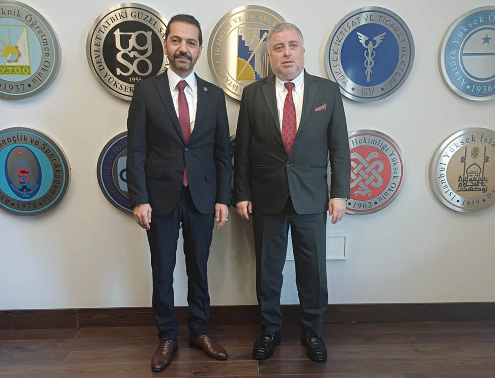 Two men in suits standing in front of a wall of plaques. Description generated by AI
