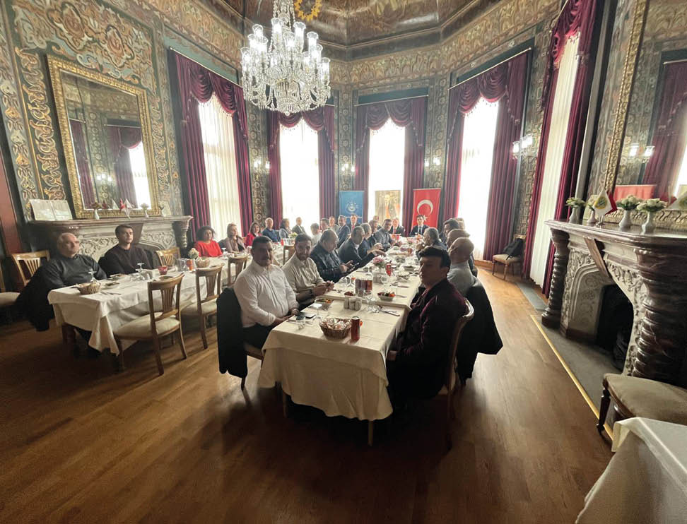 A group of people are sitting around a table in a large room. Description generated by AI