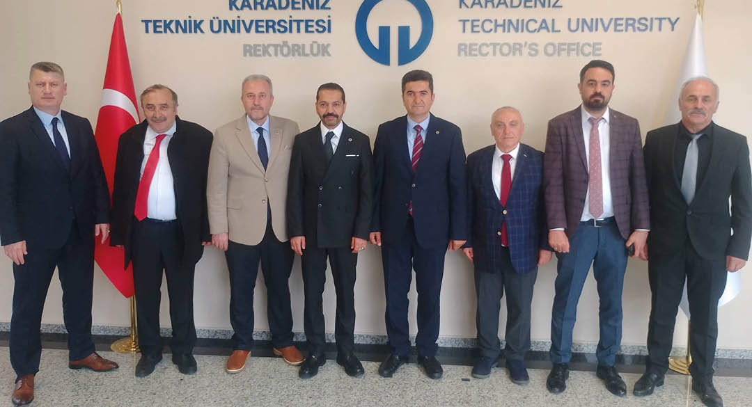 Five adults dressed in formal attire stand side by side in front of a wall with text and a logo related to a university rector's office. Description generated by AI