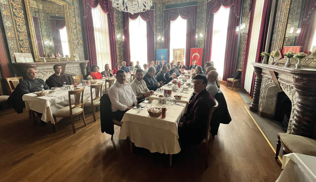 A group of people are sitting around a table in a large room. Description generated by AI