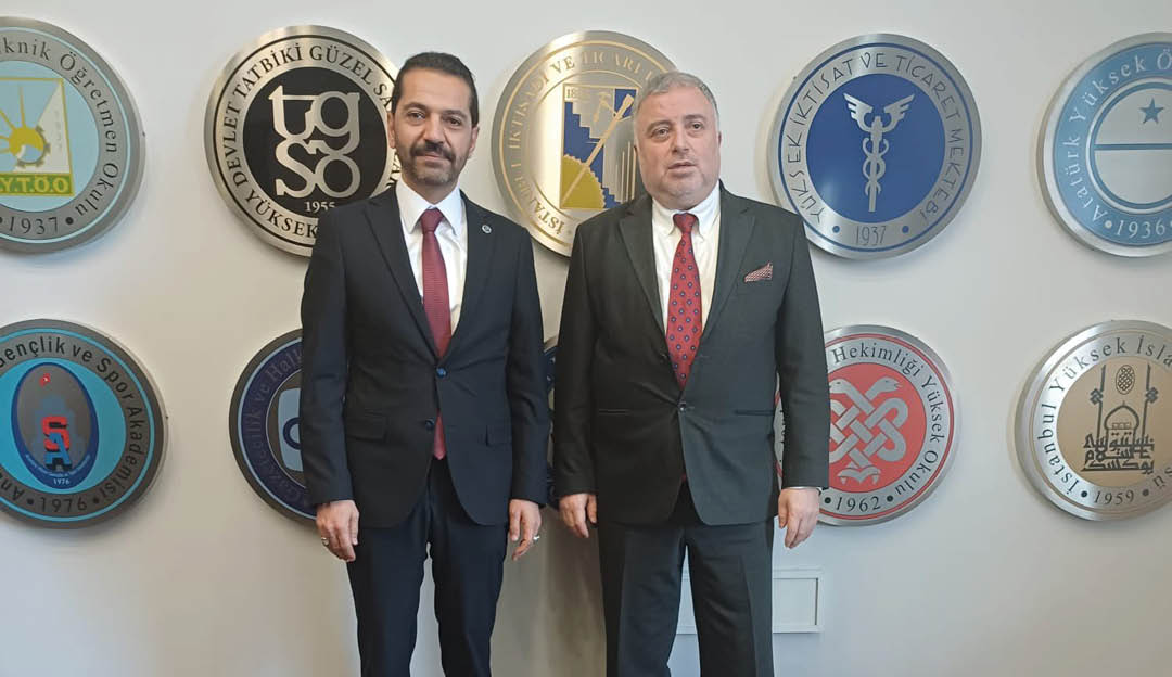 Two men in suits standing in front of a wall of plaques. Description generated by AI