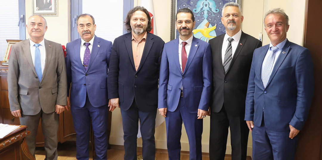 Four adults wearing formal suits stand side by side indoors with a colorful painting visible in the background. Description generated by AI